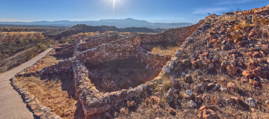 A panoramic view of Tuzigoot National Monument, showcasing the expansive ancient pueblo ruins perched on a hilltop. The stone structures stretch across the ridge, with the Verde Valley's lush greenery and distant mountains forming a breathtaking backdrop.