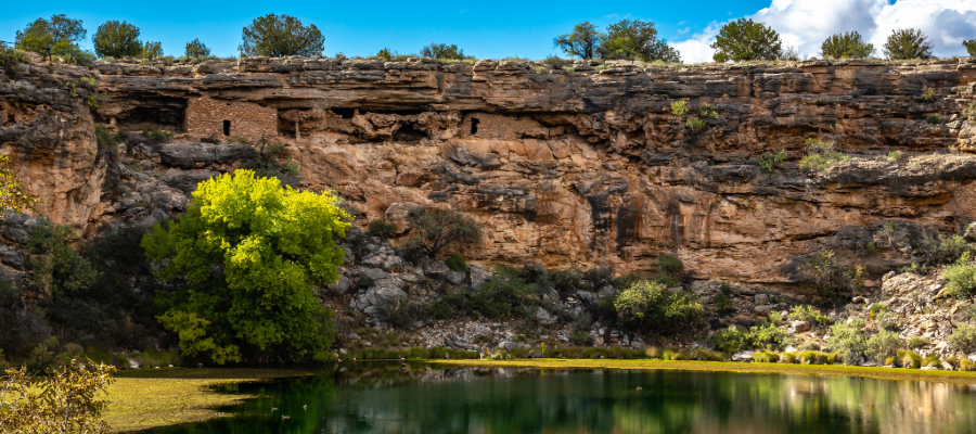"Panoramic view of Montezuma Well, a natural limestone sinkhole in Arizona, surrounded by lush vegetation and ancient Sinagua cliff dwellings, showcasing its unique hydrology and cultural significance."