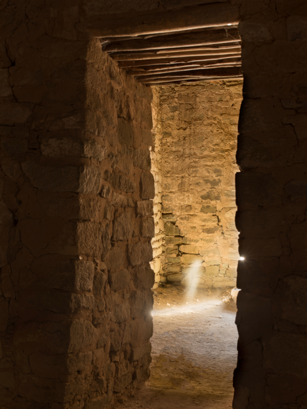 "A series of ancient stone doorways within the Aztec Ruins National Monument, constructed from rough-hewn stones and mortar, creating a tunnel-like effect with dim lighting highlighting the textured walls and uneven floor."