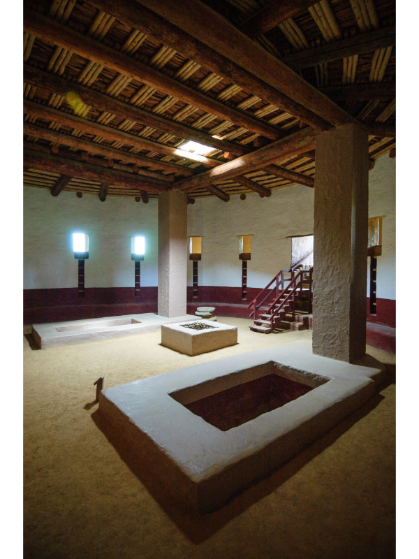 "The Great Kiva at Aztec Ruins National Monument, a circular ceremonial structure made of sandstone blocks, partially underground with wooden beams, set in an arid landscape under a clear blue sky."