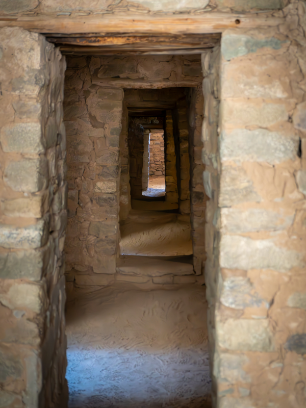 "A series of ancient stone doorways within the Aztec Ruins National Monument, constructed from rough-hewn stones and mortar, creating a tunnel-like effect with dim lighting highlighting the textured walls and uneven floor."