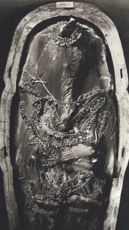 A close-up view of the second coffin of King Tutankhamun, partially covered in debris from the tomb’s interior. The image shows intricate goldwork and inlays of semi-precious stones, with symbolic iconography representing the pharaoh’s protection and afterlife journey.