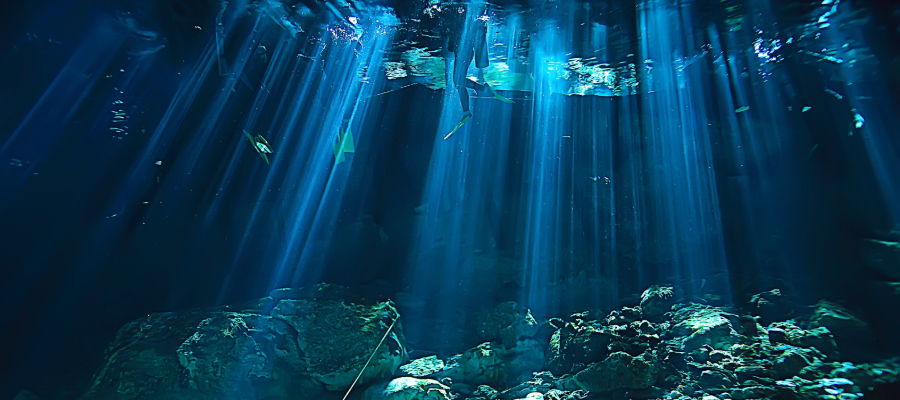 A scuba diver explores the underwater depths of a cenote in the Yucatán Peninsula, Mexico, near Tulum cenotes, surrounded by crystal-clear water, limestone formations, and beams of sunlight.