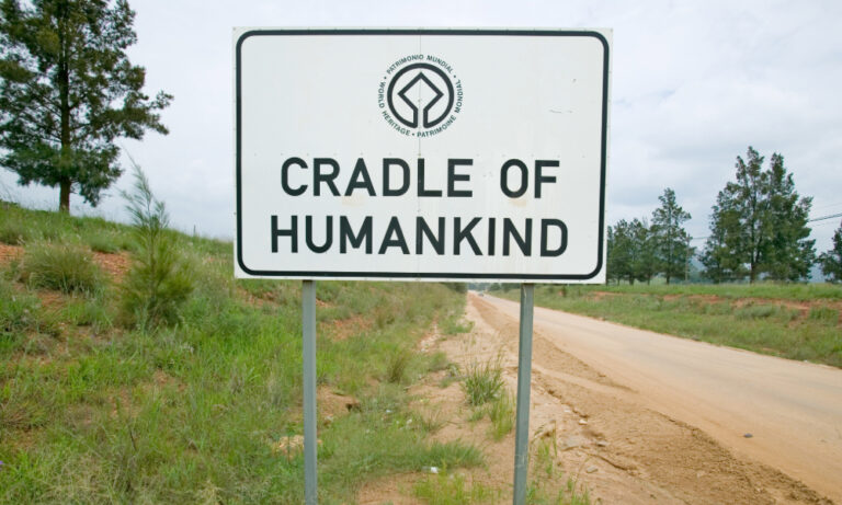 "Weather-worn 'Cradle of Humankind' sign with UNESCO World Provenance Definition: Heritage emblem, showing trilingual labeling (English/Spanish/French) at this South African paleoanthropological site where early hominin fossils were discovered in limestone caves."
