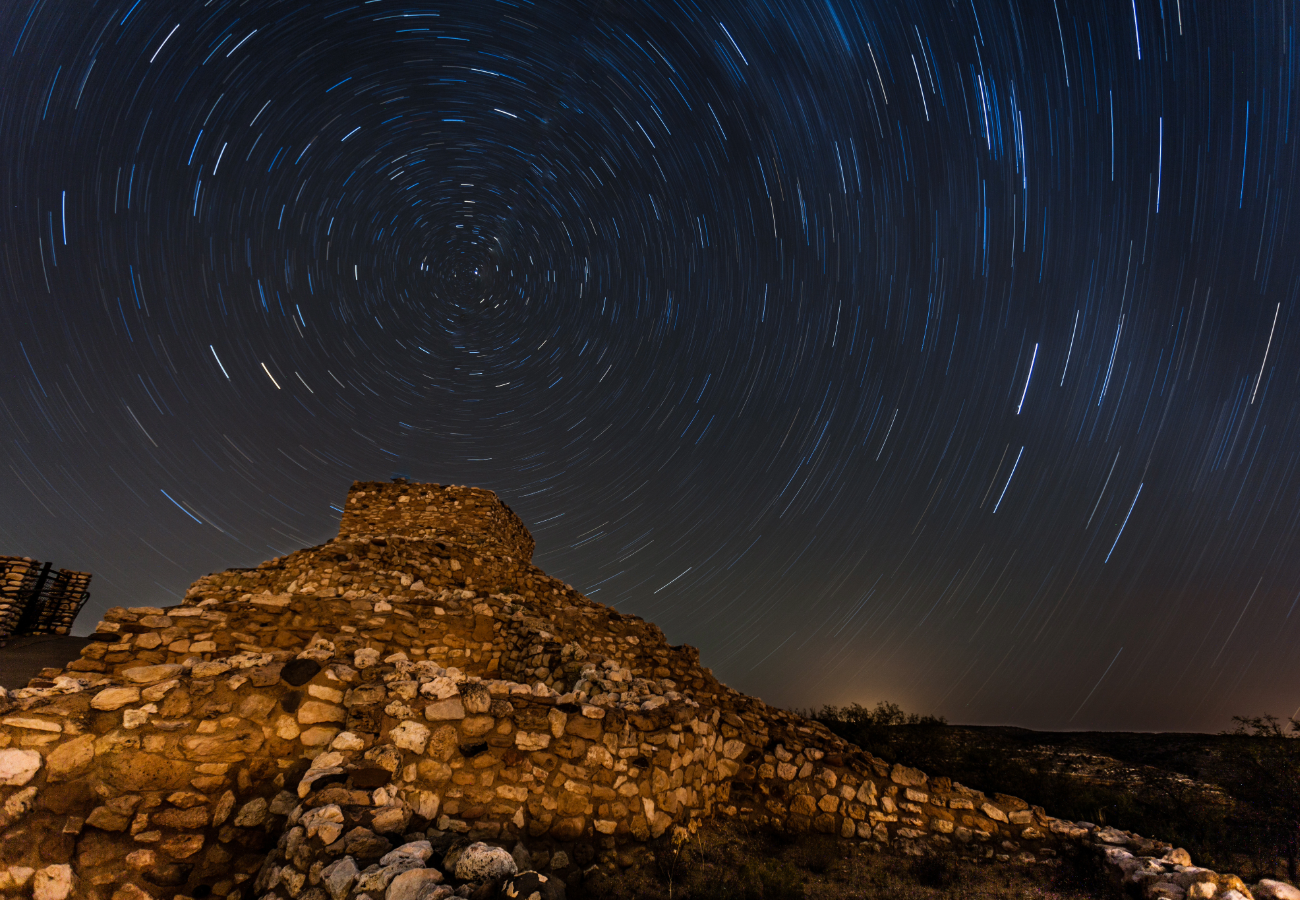 ground-level view of Tuzigoot National Monument, an ancient Sinagua pueblo ruin perched on a hilltop in the Verde Valley, Arizona. The stone structures overlook a scenic landscape of desert vegetation, green valleys, and distant mountains