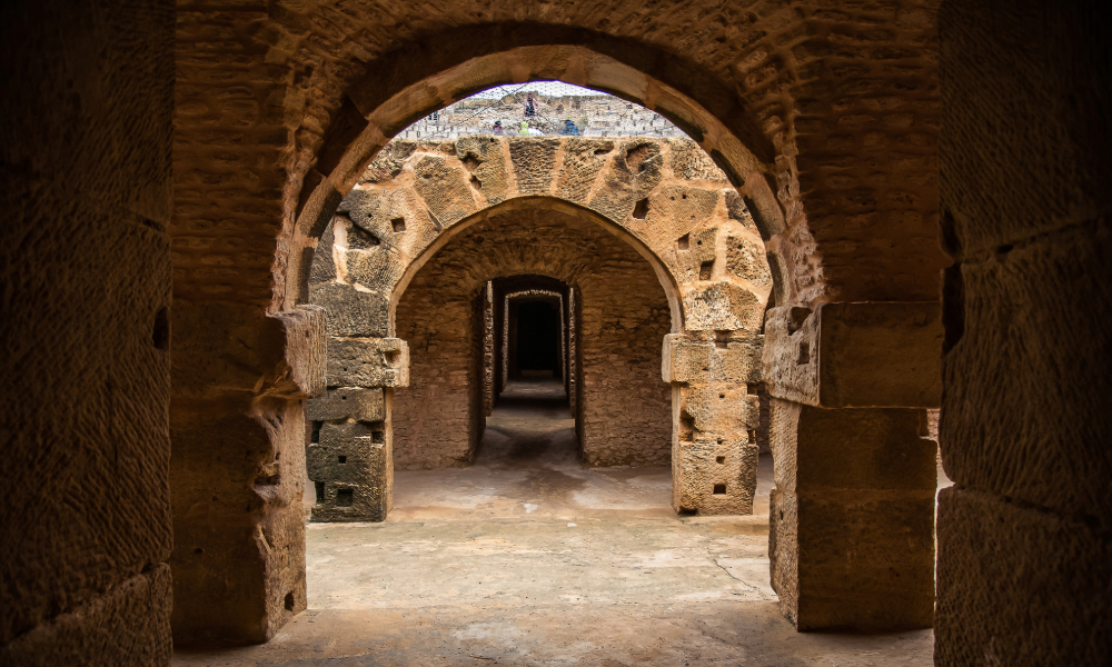 Restoration Definition: *"Sunlit Roman arches at Uthina archaeological site in Tunisia, showing well-preserved brick-and-stone construction from the 1st century CE Augustus-era colony, with arid hills in the background."*