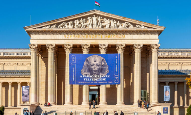 "Daytime view of Budapest's Museum of Fine Arts with a large 'Discovery of the Pharaoh's Tomb' exhibition banner featuring Tutankhamun's image, Hungarian flag flying above its neoclassical columns." Definition of Exhibition