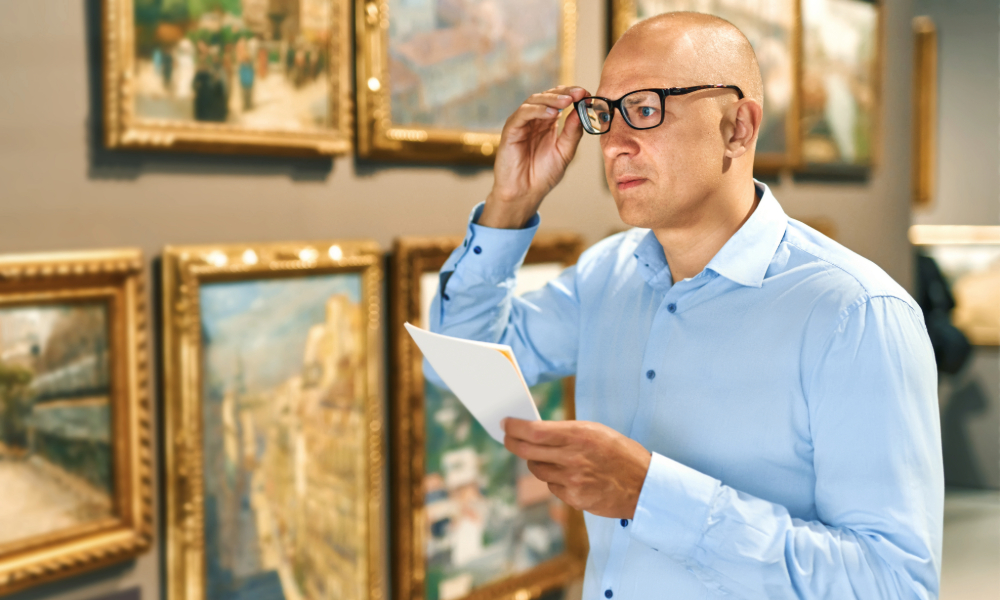 *"A man in an art gallery studies a wall of framed 19th-century landscape paintings while holding a printed guide."* Art Collection Definition