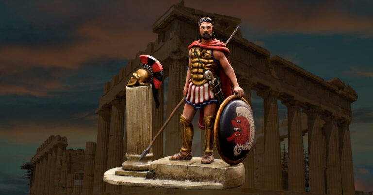 A fully equipped Greek hoplite stands ready for battle, wearing a bronze muscle cuirass and Corinthian helmet, holding a dory spear and aspis shield adorned with a lambda emblem, with bronze greaves protecting his legs.