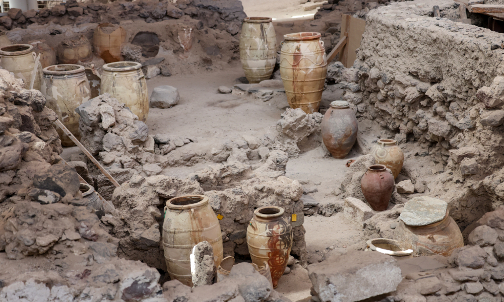 "Archaeologists carefully excavate an ancient site using trowels and brushes, uncovering artifacts and skeletal remains in stratified soil layers under a bright sun. Team members document findings with cameras and notebooks."